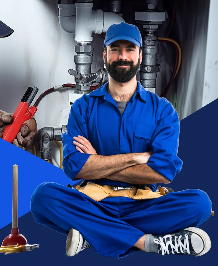 Smiling Plumbera plumber in blue overalls sitting cross-legged in front of pipes